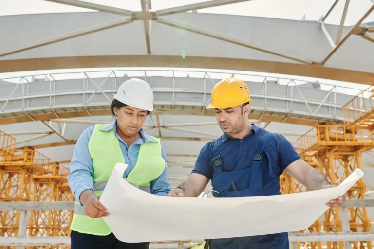 Baretli iki çalışan şantiyede plan inceliyor: asıl işveren ve alt işveren sorumluluğu
