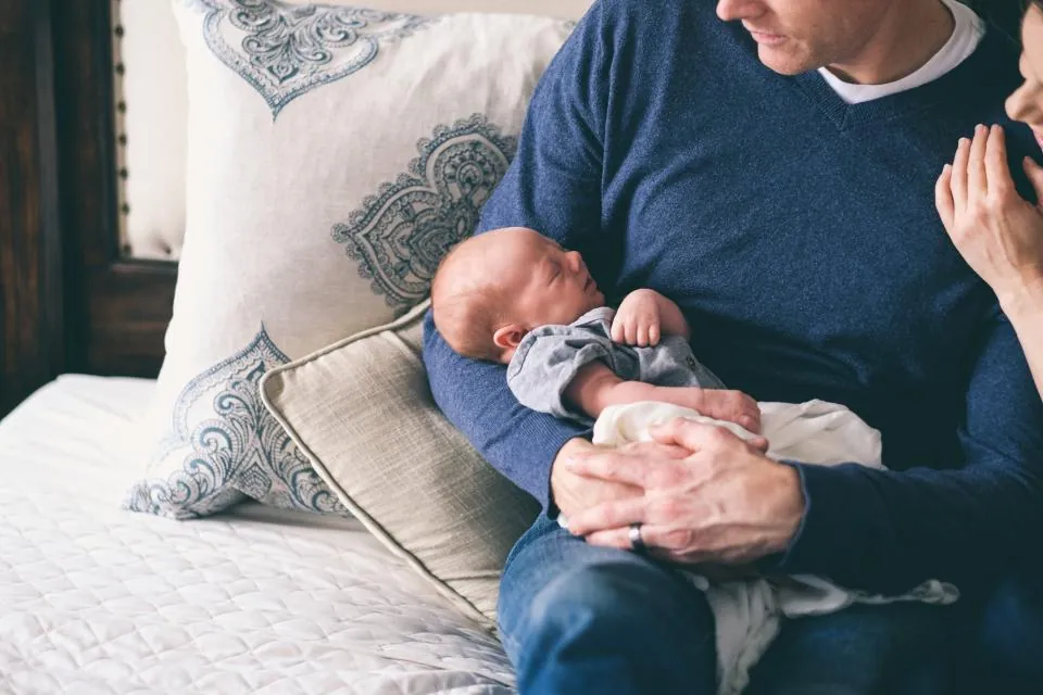 Yatakta yeni doğmuş bebeğini kucağında tutan baba