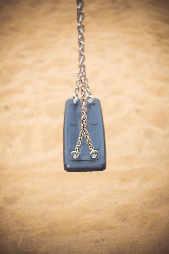 Illustrative childhood image of an empty swing standing on sand
