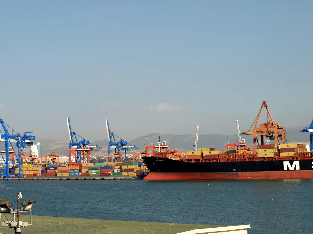İzmir körfezinde liman vinçleri ve yük gemisi, birleşen şirketlerin ticari faaliyetini simgeleyen görünüm