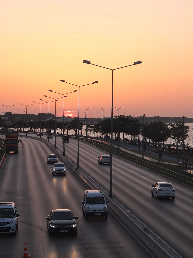 Gün batımında körfez boyunca uzanan sahil yolunda araç trafiği