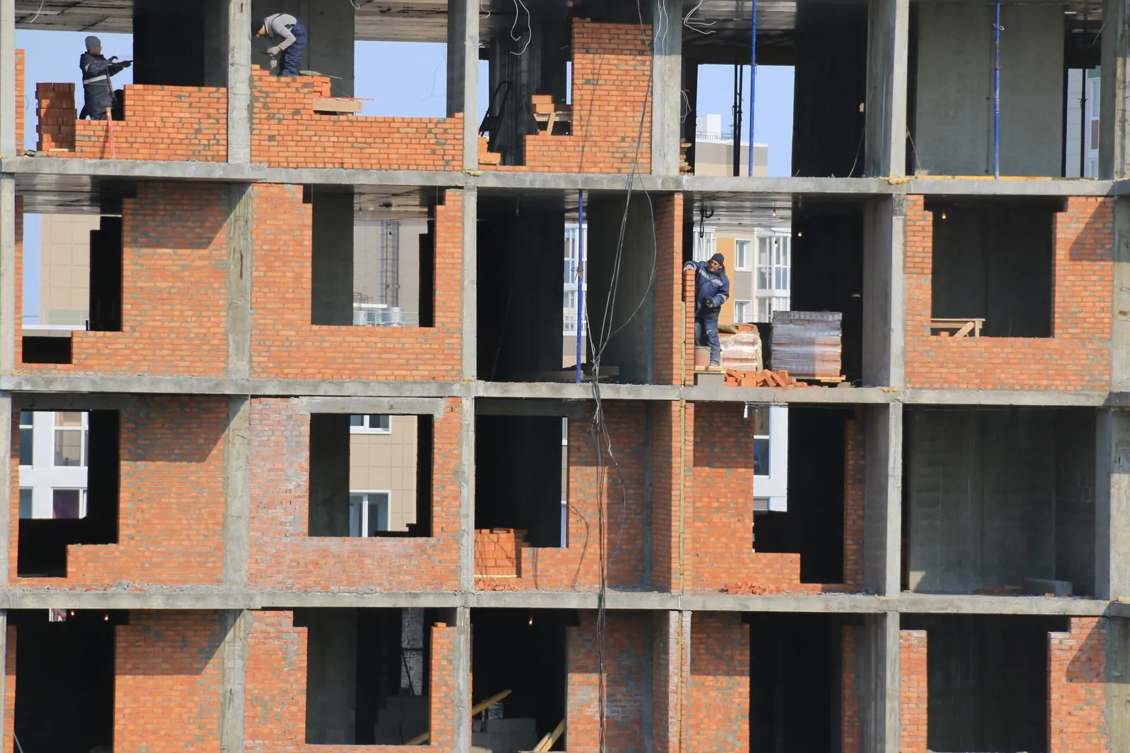 Betonarme iskelet içinde tuğla duvar ören işçilerin bulunduğu inşaat